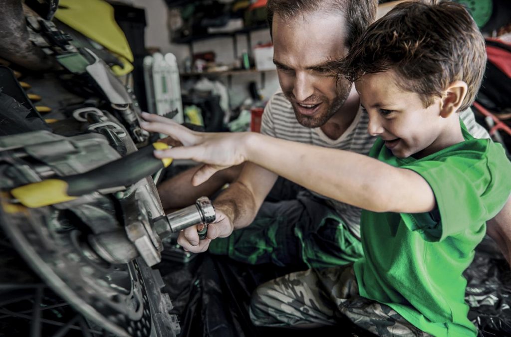 A boy helping his dad with fixing a motorcycle in the garage